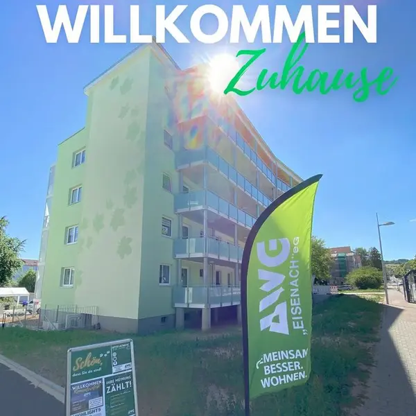 Wohngebäude mit "Willkommen Zuhause"-Fahne, strahlender Sonnenschein